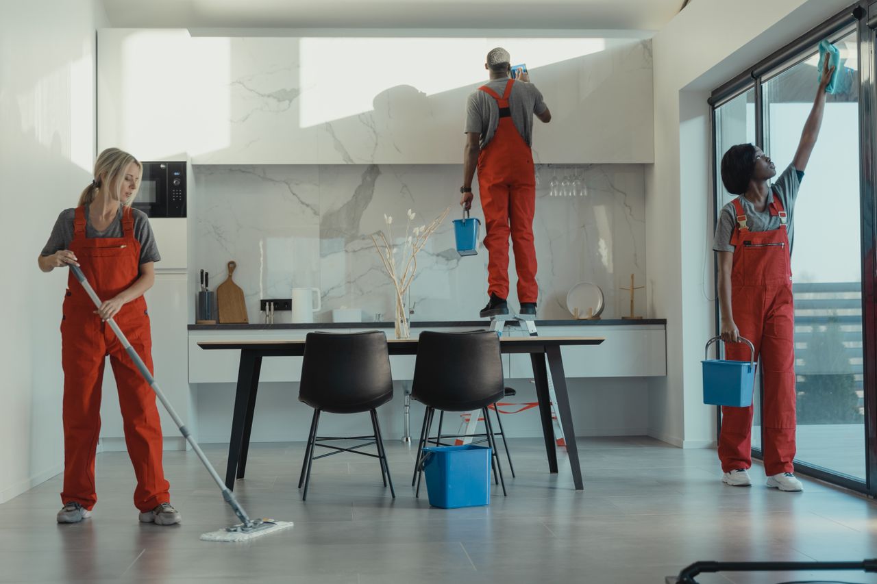 Un groupe de nettoyeurs en uniformes rouges passe la serpillière et essuie les vitres dans une salle à manger moderne.